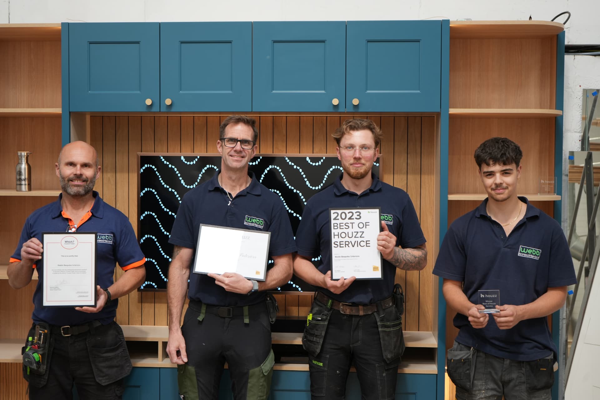 The Webb Bespoke Interiors team, four craftsmen in branded polo shirts holding their Which? Trusted Trader and Houzz awards in front of a bespoke fitted media unit