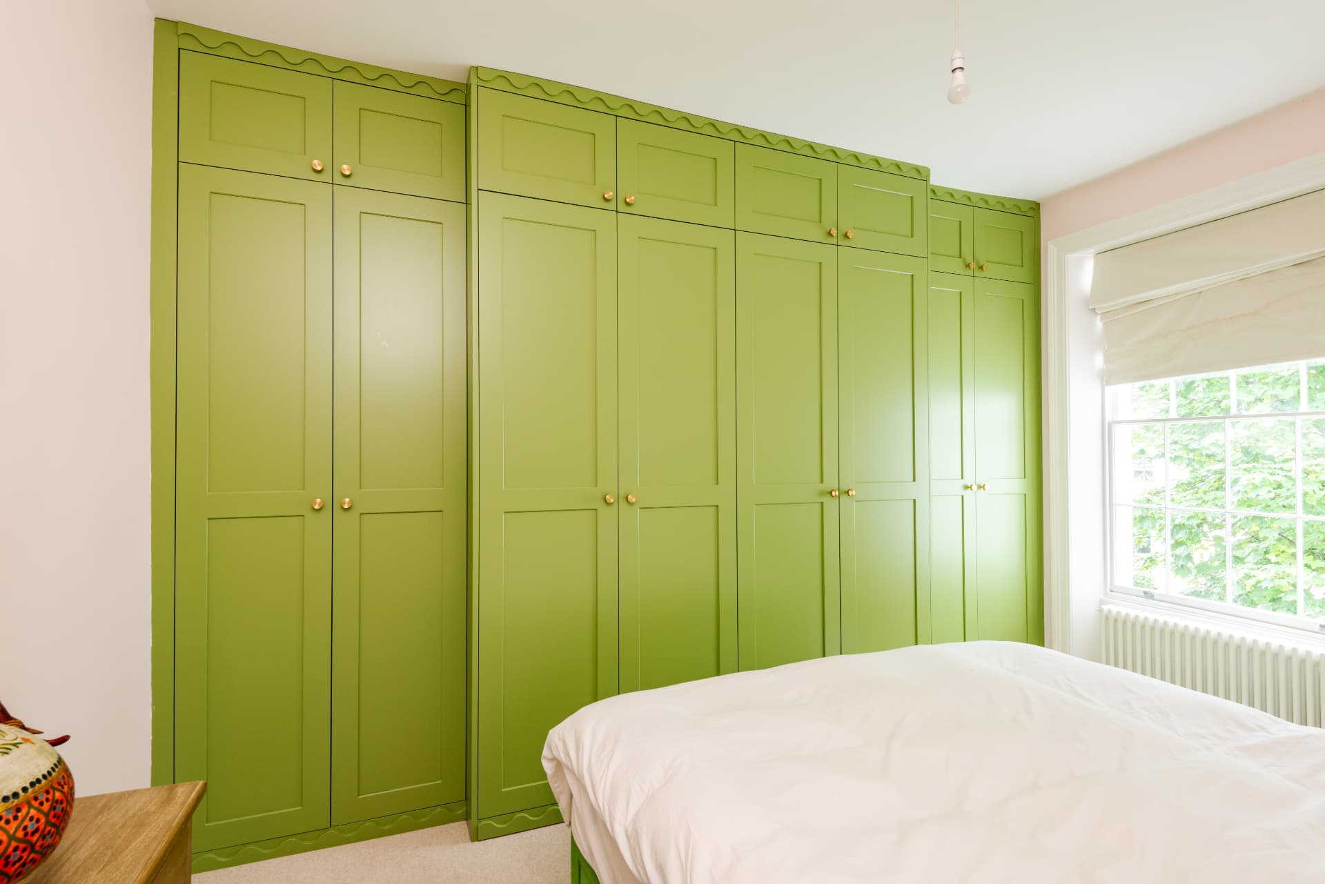 Floor-to-ceiling green shaker wardrobes fitted across a bedroom wall